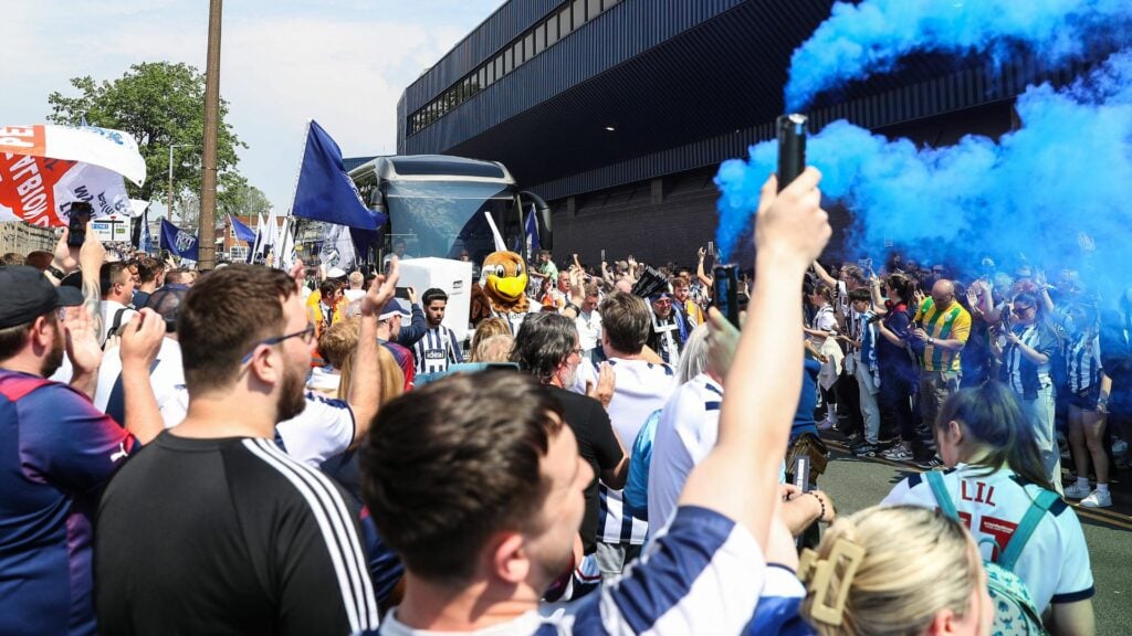 West Brom fans welcome the team bus at The Hawthorns, as one supporter holds up a blue flare.