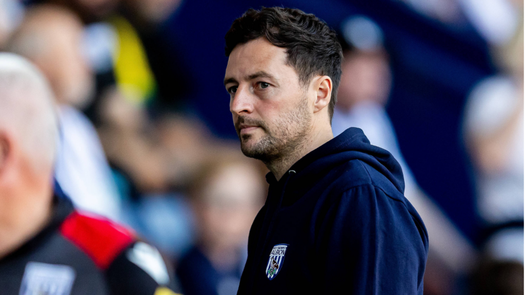 West Brom manager Ryan Mason stares into the distance while wearing a club hoodie on the touchline.